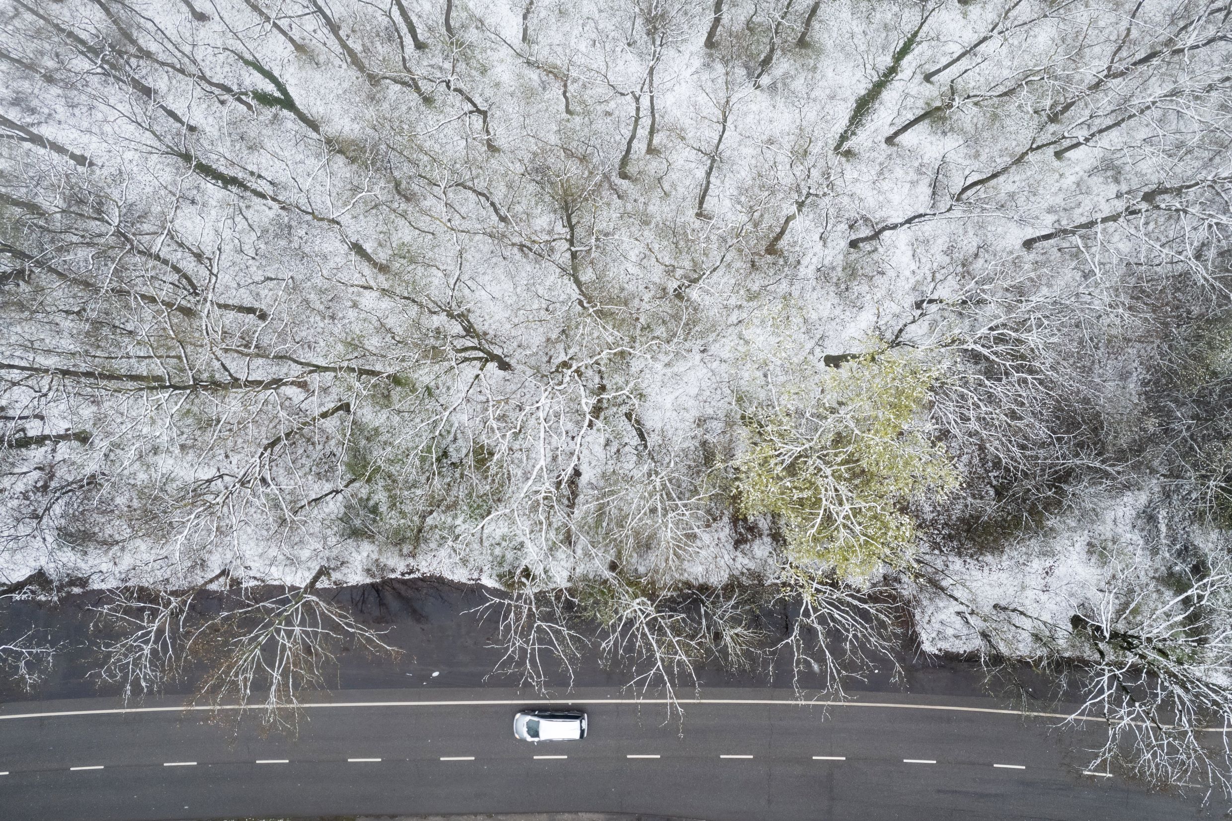 A drónnal készített képen autó az úton egy behavazott erdő mellett Debrecenben 2023. április 7-én.