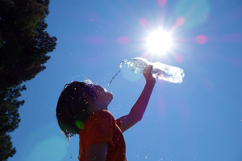Egy gyerek vizet önt magába egy műanyag palackból a szikrázó napsütésben.