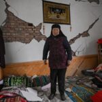 A földrengés során megrongálódott házában áll egy nő.