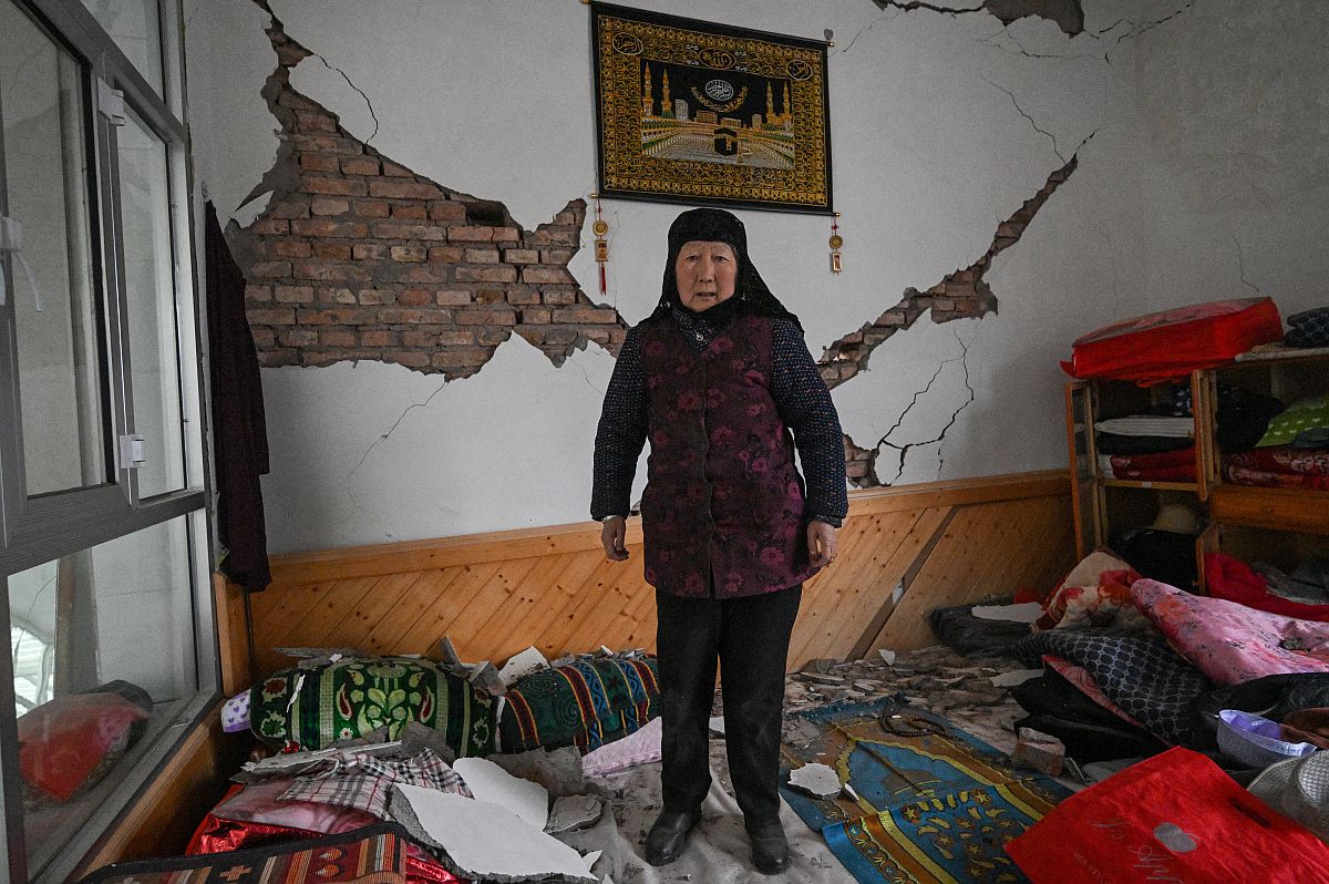 A földrengés során megrongálódott házában áll egy nő.